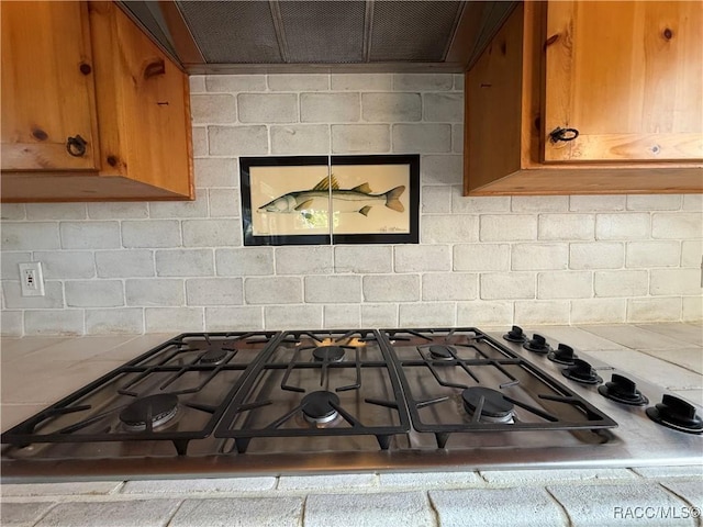 5217 Riverside Dr, Yankeetown, FL 34498 - kitchen view of stainless steel gas cooktop, brown cabinetry, extractor fan, and backsplash