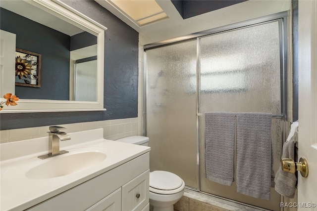 bathroom featuring vanity, toilet, walk in shower, and tile walls