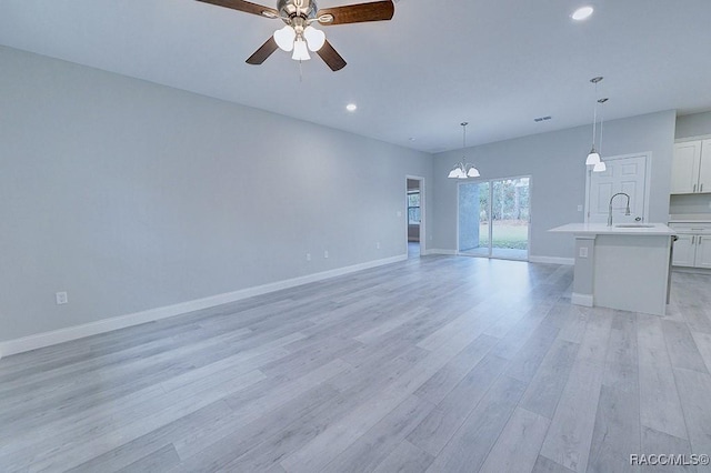 unfurnished living room featuring ceiling fan with notable chandelier, light hardwood / wood-style flooring, and sink