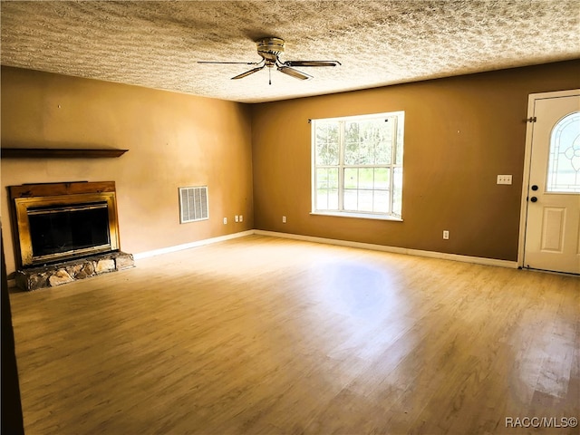 unfurnished living room with a textured ceiling, ceiling fan, a fireplace, and light hardwood / wood-style flooring