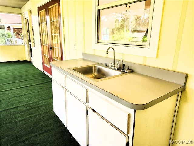 kitchen with dark carpet, white cabinetry, and sink