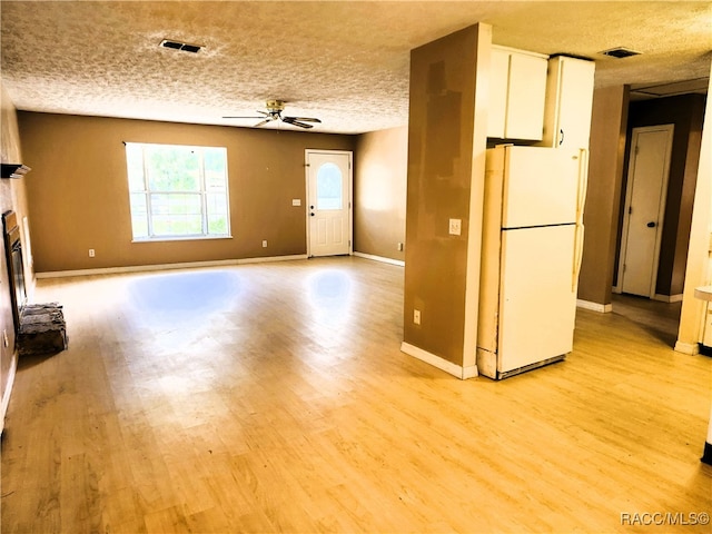 unfurnished living room featuring ceiling fan, light wood-type flooring, a textured ceiling, and a brick fireplace