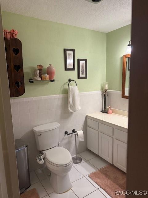 half bathroom with tile patterned flooring, vanity, wainscoting, toilet, and a textured ceiling