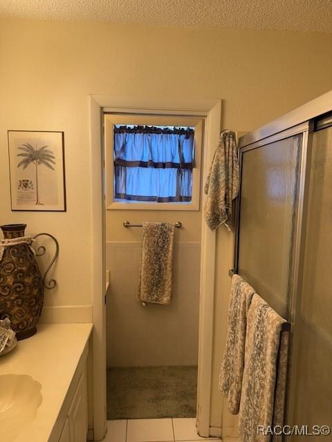 bathroom featuring a shower with door, a textured ceiling, tile patterned flooring, and vanity