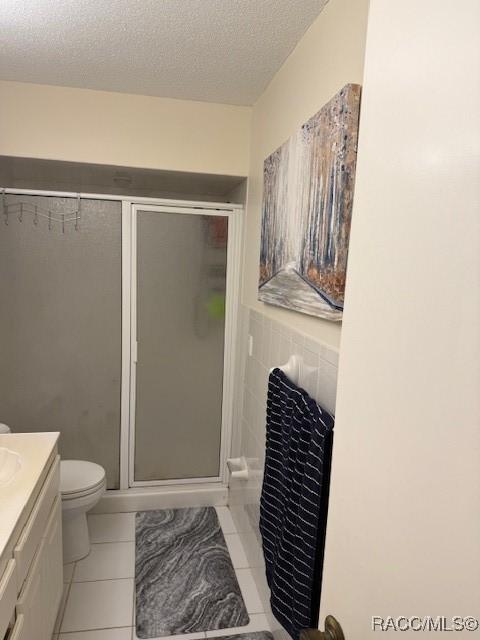 full bathroom featuring vanity, toilet, a textured ceiling, tile patterned floors, and a shower stall