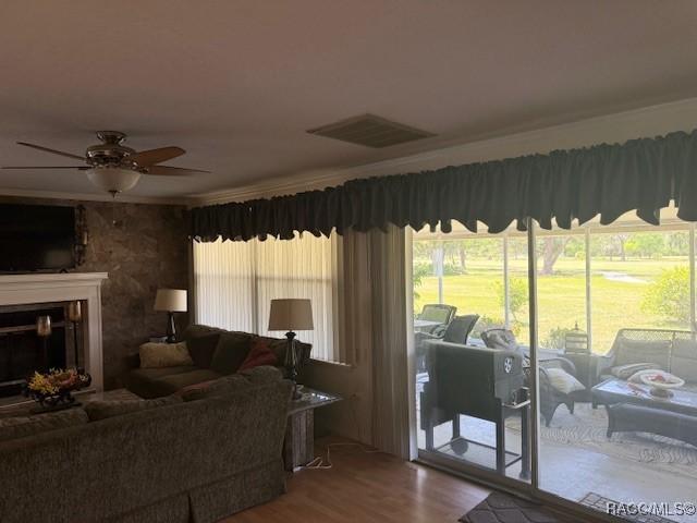 living area featuring ceiling fan, a fireplace, wood finished floors, and visible vents