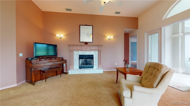 living area with light colored carpet, a ceiling fan, visible vents, and a high end fireplace