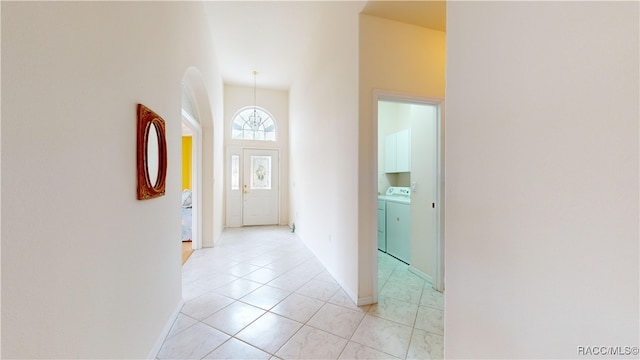 corridor featuring light tile patterned floors, baseboards, independent washer and dryer, and a towering ceiling