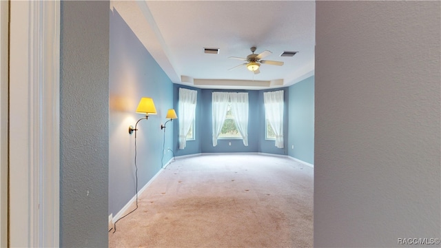 carpeted empty room featuring a tray ceiling, baseboards, visible vents, and ceiling fan