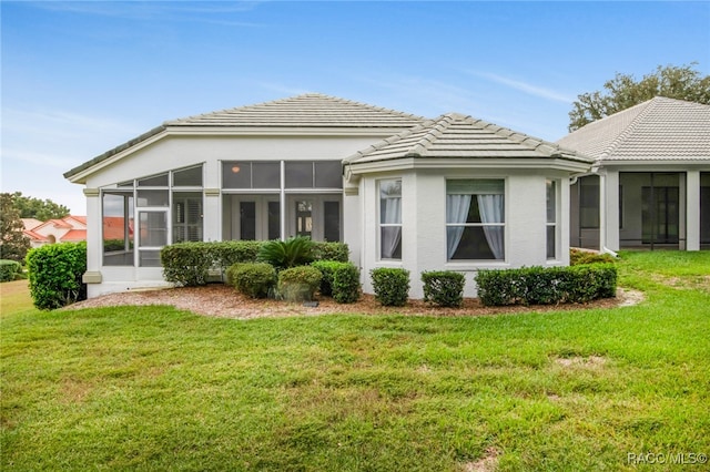 back of property featuring a tiled roof, a lawn, a sunroom, and stucco siding