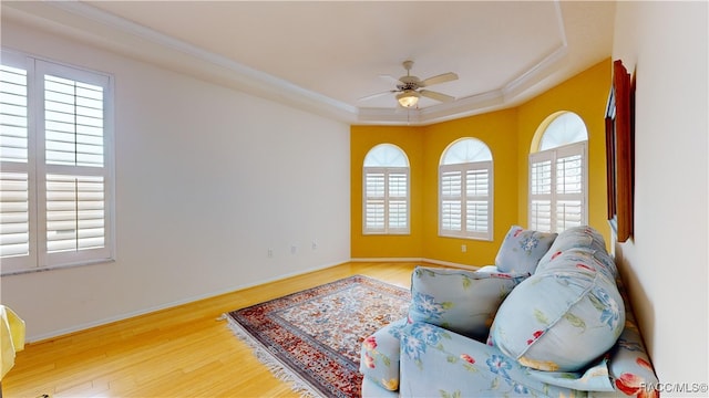 living area with wood finished floors, baseboards, ceiling fan, ornamental molding, and a raised ceiling