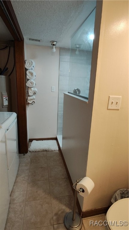 bathroom with a textured ceiling, water heater, separate washer and dryer, tile patterned flooring, and toilet