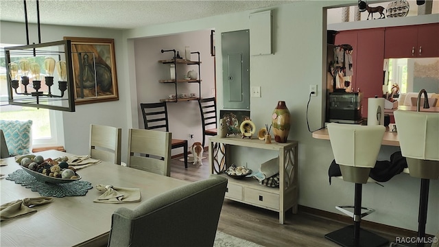 dining space featuring electric panel, dark wood-type flooring, a textured ceiling, and an inviting chandelier