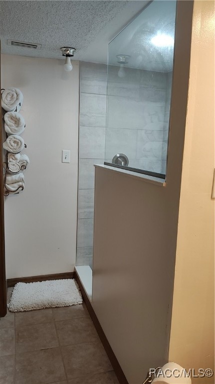 bathroom with a textured ceiling, walk in shower, and tile patterned floors