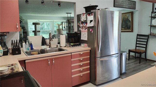 kitchen featuring a textured ceiling, sink, range, light hardwood / wood-style floors, and stainless steel refrigerator