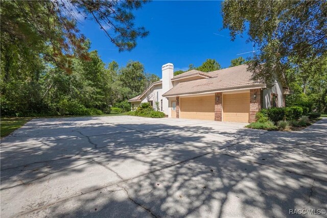 5550 W Yearling Dr, Beverly Hills, FL 34465 - view of side of property featuring a tile roof, driveway, an attached garage, brick siding, and a chimney