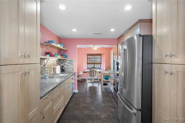 kitchen featuring backsplash, ceiling fan, dark stone countertops, light brown cabinetry, and stainless steel appliances