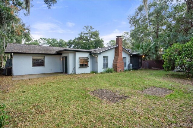 927 Cedar Ave, Inverness, FL 34452 - back of property with stucco siding, a chimney, and a yard