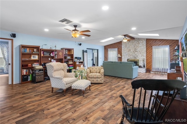 living room with a fireplace, ceiling fan, vaulted ceiling with skylight, and wood-type flooring