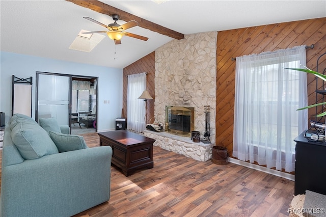 living room featuring vaulted ceiling with skylight, ceiling fan, wooden walls, wood-type flooring, and a fireplace