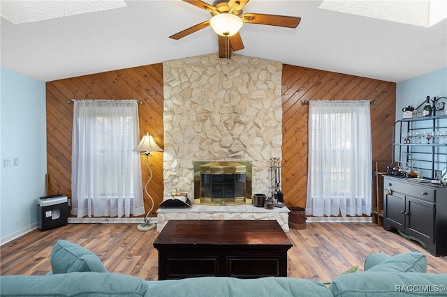 living room with vaulted ceiling with skylight, a fireplace, wood walls, and hardwood / wood-style floors