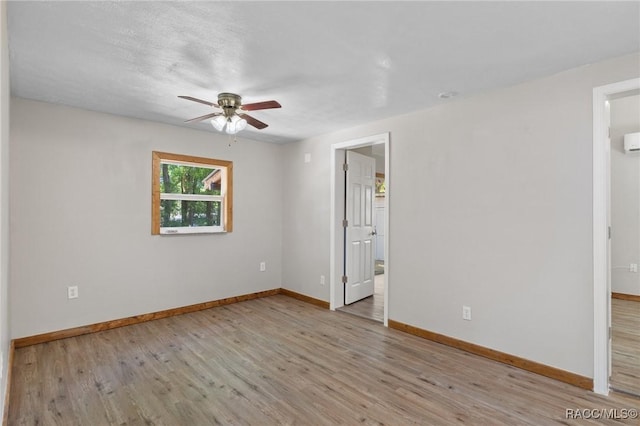 spare room featuring baseboards, ceiling fan, wood finished floors, and a wall unit AC
