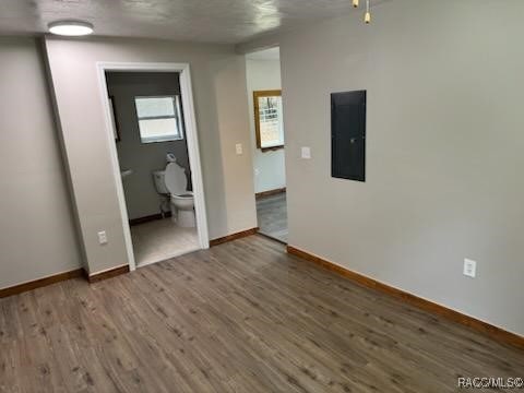 unfurnished room with a textured ceiling, electric panel, and dark hardwood / wood-style floors