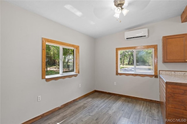 unfurnished dining area with plenty of natural light, baseboards, a wall mounted air conditioner, and light wood-style flooring