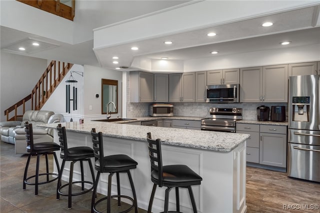 kitchen featuring kitchen peninsula, appliances with stainless steel finishes, a kitchen breakfast bar, light stone counters, and gray cabinetry