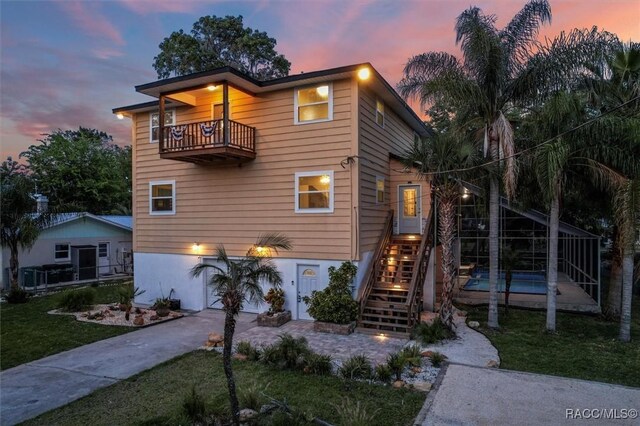 back house at dusk with glass enclosure, ceiling fan, and a lawn