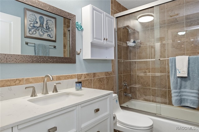 full bathroom with vanity, toilet, tile walls, and bath / shower combo with glass door