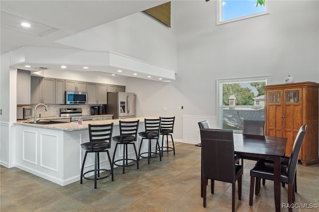 kitchen featuring light stone countertops, sink, stainless steel appliances, tasteful backsplash, and gray cabinets