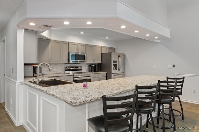 kitchen with gray cabinetry, a breakfast bar, sink, appliances with stainless steel finishes, and kitchen peninsula