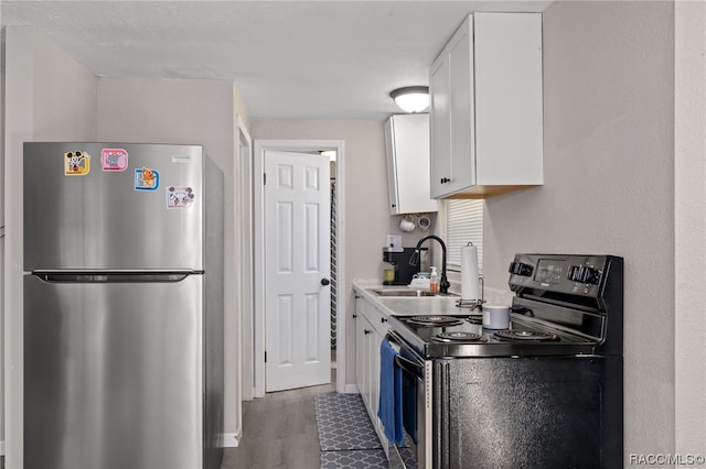 kitchen with stainless steel fridge, white cabinetry, black range with electric stovetop, and sink