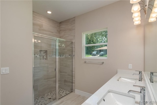 bathroom featuring double vanity, baseboards, a shower stall, and a sink