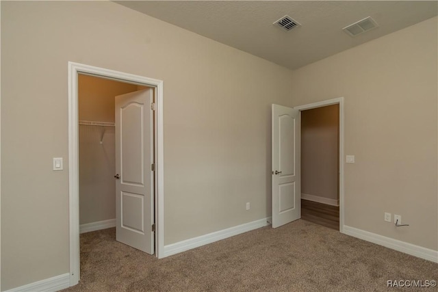 unfurnished bedroom with a spacious closet, carpet flooring, and visible vents