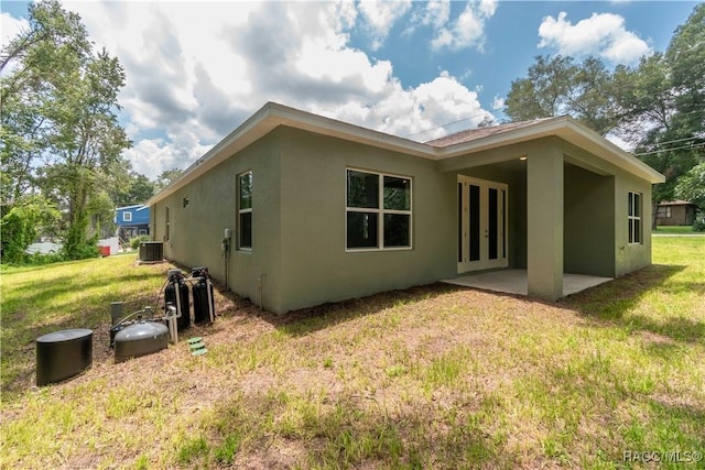 rear view of property with central air condition unit, stucco siding, a yard, and a patio area