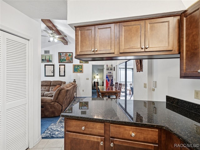 kitchen featuring beamed ceiling, light tile patterned floors, ceiling fan, and dark stone counters