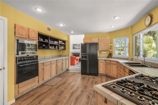 kitchen with tile countertops, visible vents, open shelves, a sink, and black appliances
