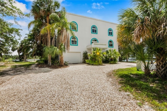 view of front of house with an attached garage, stucco siding, and gravel driveway