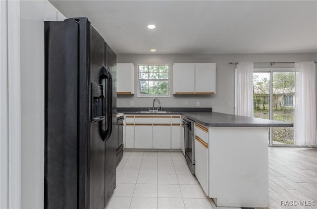 kitchen featuring dark countertops, a peninsula, black appliances, white cabinetry, and a sink