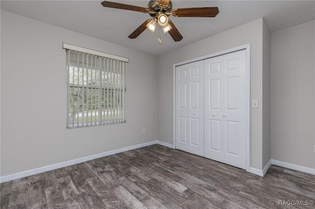 unfurnished bedroom featuring dark wood-style floors, a closet, baseboards, and a ceiling fan