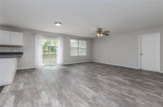 unfurnished living room with ceiling fan, baseboards, and wood finished floors