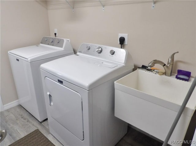 clothes washing area with sink, light hardwood / wood-style flooring, and washing machine and clothes dryer