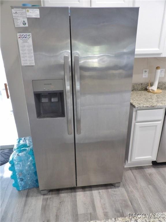 kitchen featuring stainless steel fridge, light stone countertops, light hardwood / wood-style flooring, and white cabinets