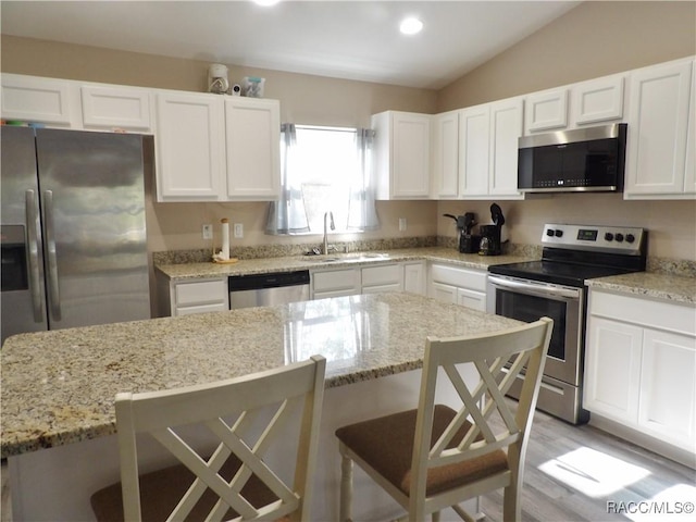 kitchen featuring a breakfast bar, white cabinetry, sink, stainless steel appliances, and light stone countertops