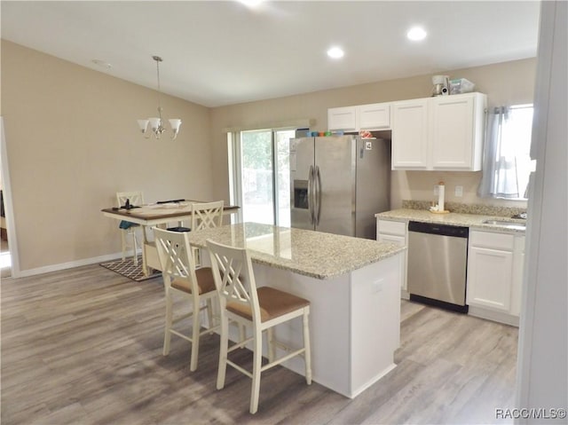 kitchen featuring light hardwood / wood-style flooring, hanging light fixtures, appliances with stainless steel finishes, a kitchen island, and white cabinets