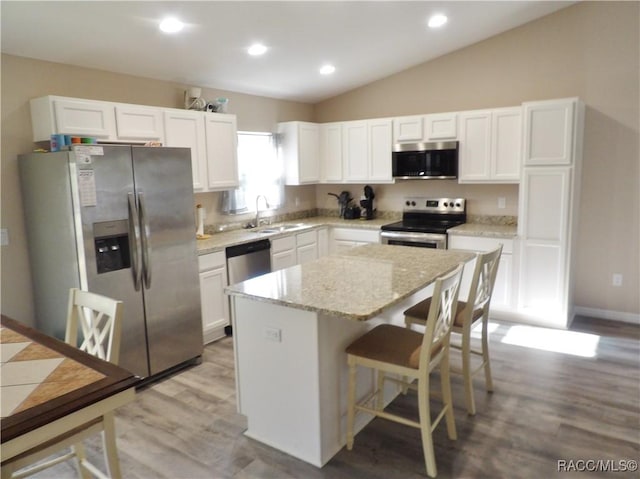 kitchen featuring white cabinetry, stainless steel appliances, light stone countertops, and a kitchen island