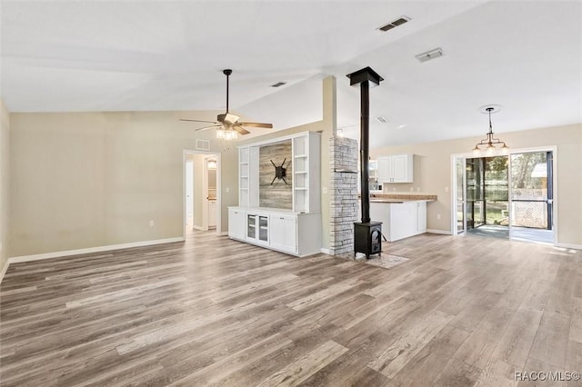 unfurnished living room featuring ceiling fan, lofted ceiling, a wood stove, and light hardwood / wood-style floors