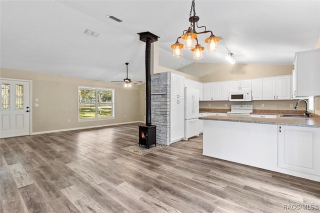 kitchen featuring pendant lighting, sink, white appliances, white cabinets, and a wood stove